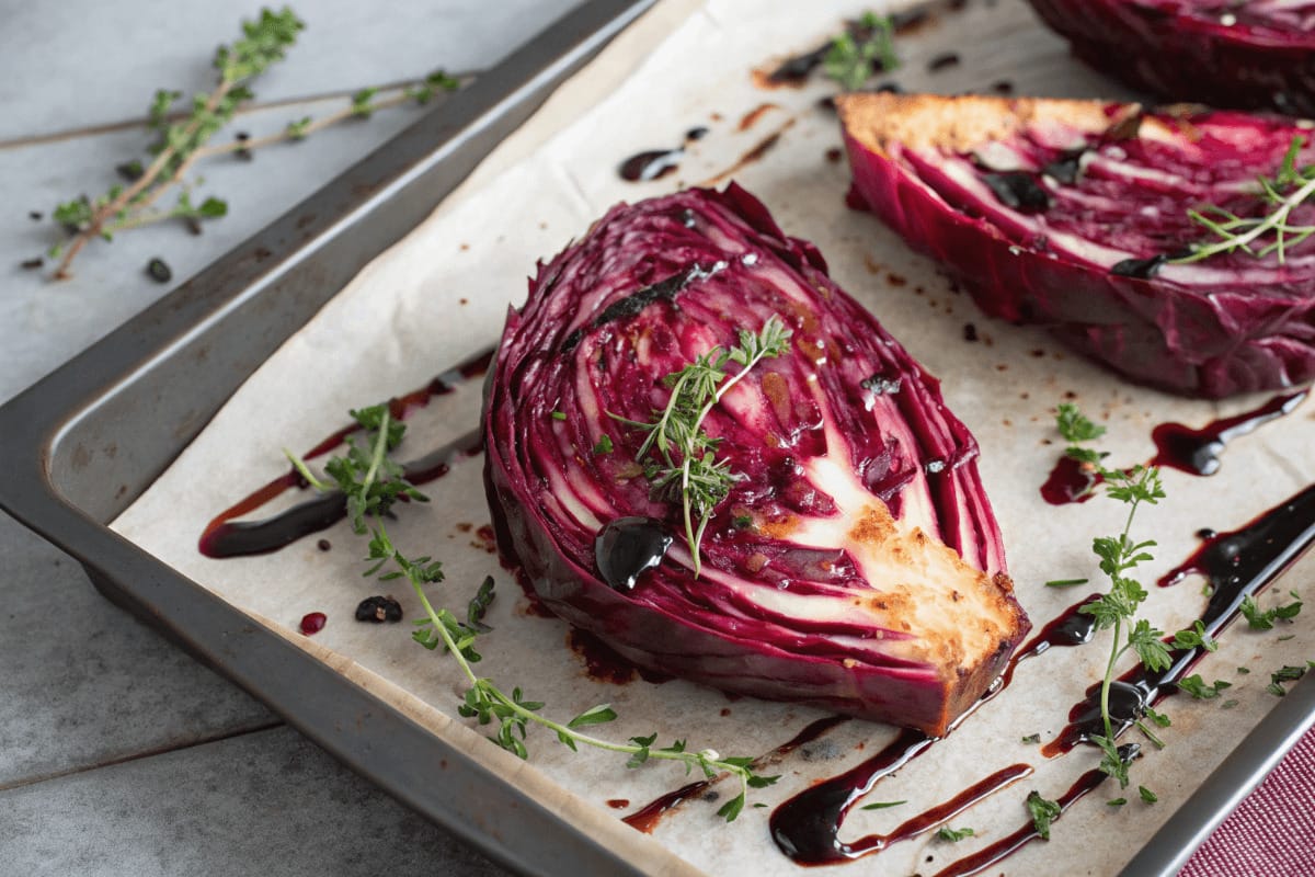 A beautifully roasted red cabbage sliced into wedges, with a crispy caramelized exterior, garnished with fresh herbs